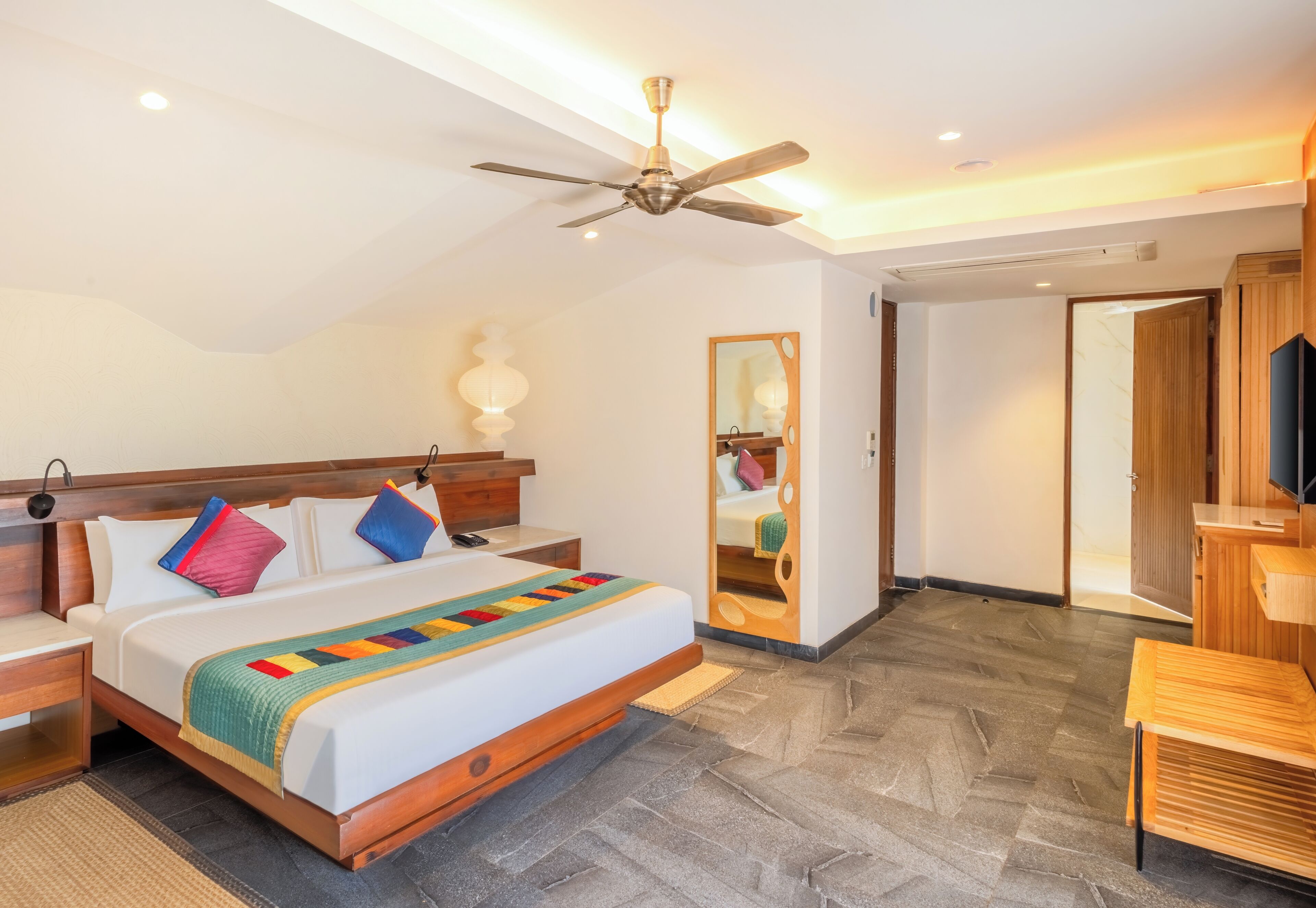 Une chambre d’hôtel équipée d’un lit, d’une table de chevet, d’une commode et d’un ventilateur de plafond.