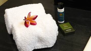 A neatly folded white towel with a flower on it, a bottle of hand soap, and a box of soap on a dark surface.