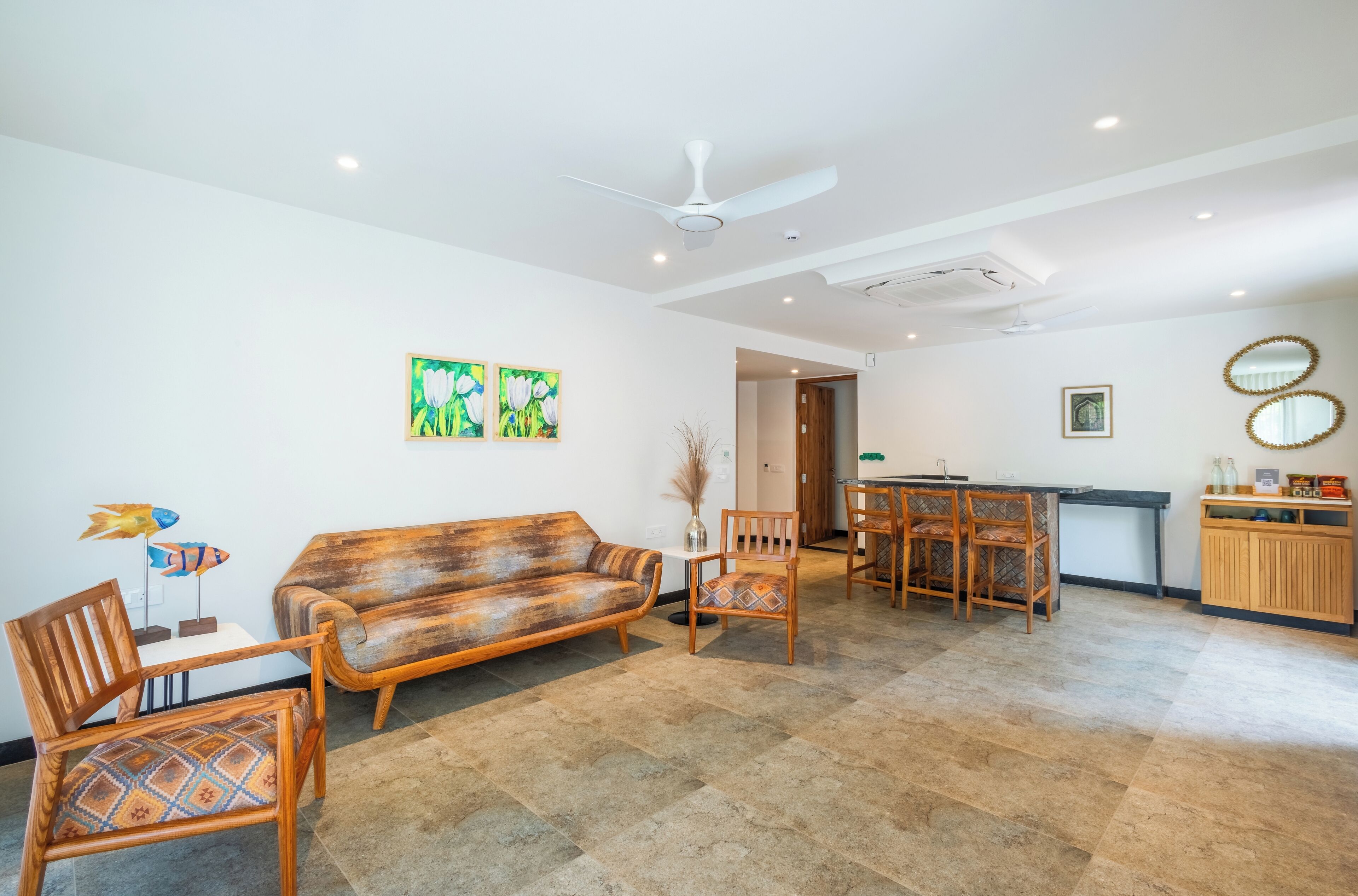 A spacious living area with a wooden sofa, two chairs, a dining table, and a kitchen area with a counter and cabinets.