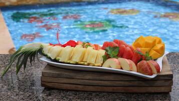 A fruit platter on a wooden board by a pool with a colorful mosaic tile background.