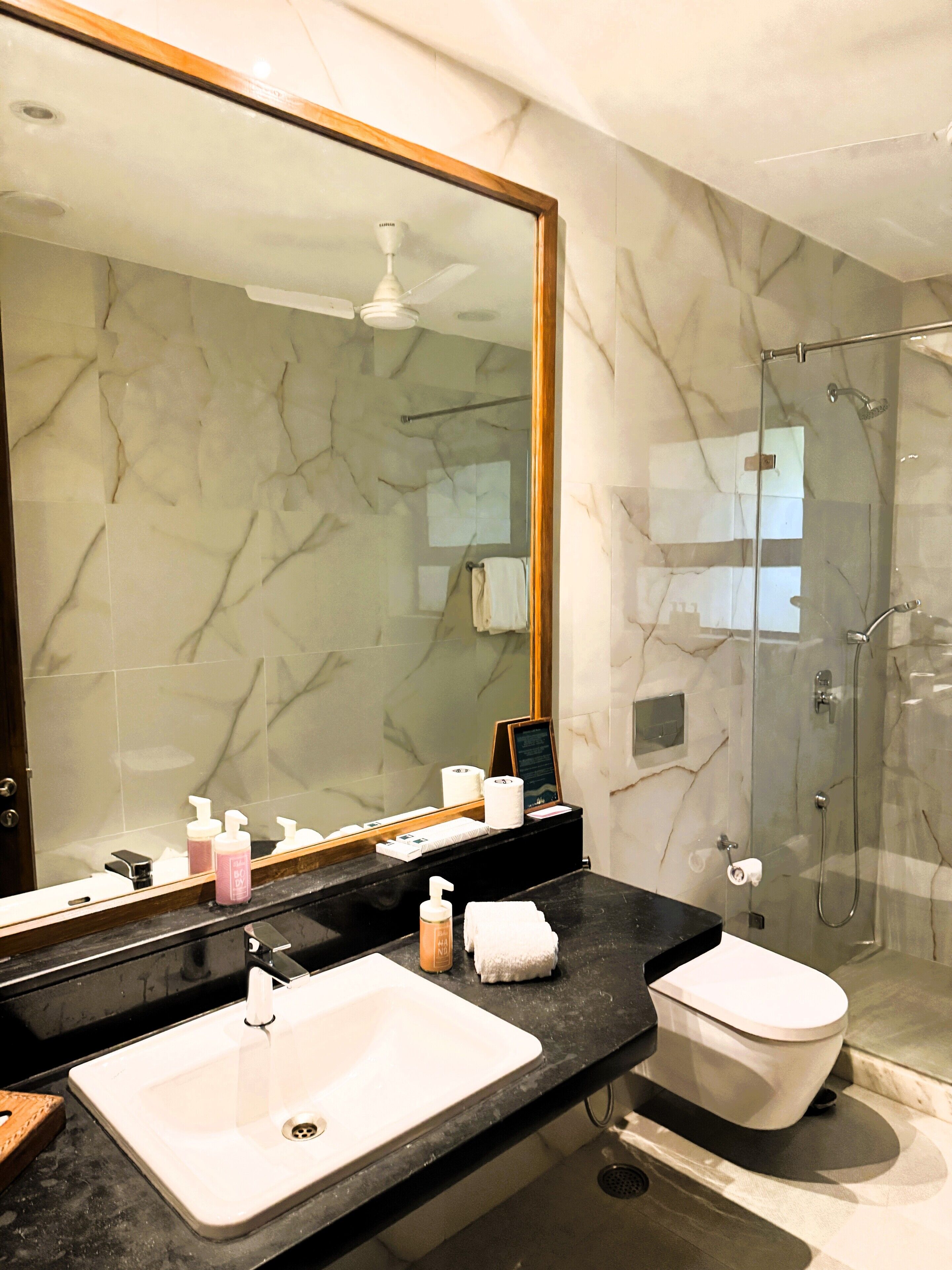 A bathroom with a large mirror, a sink, a toilet, and a shower.