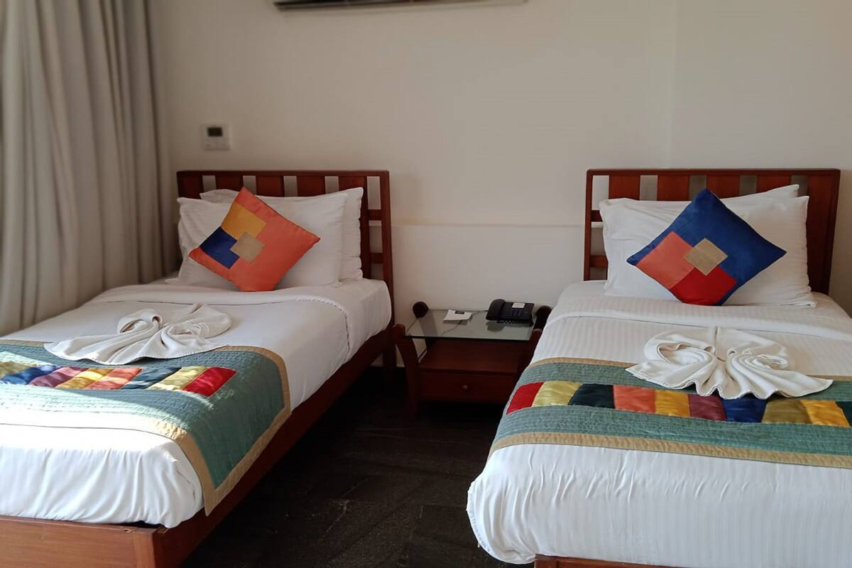 Two twin beds with white linens, colorful quilts, and decorative pillows. Each bed has a small bedside table with a phone and a lamp.