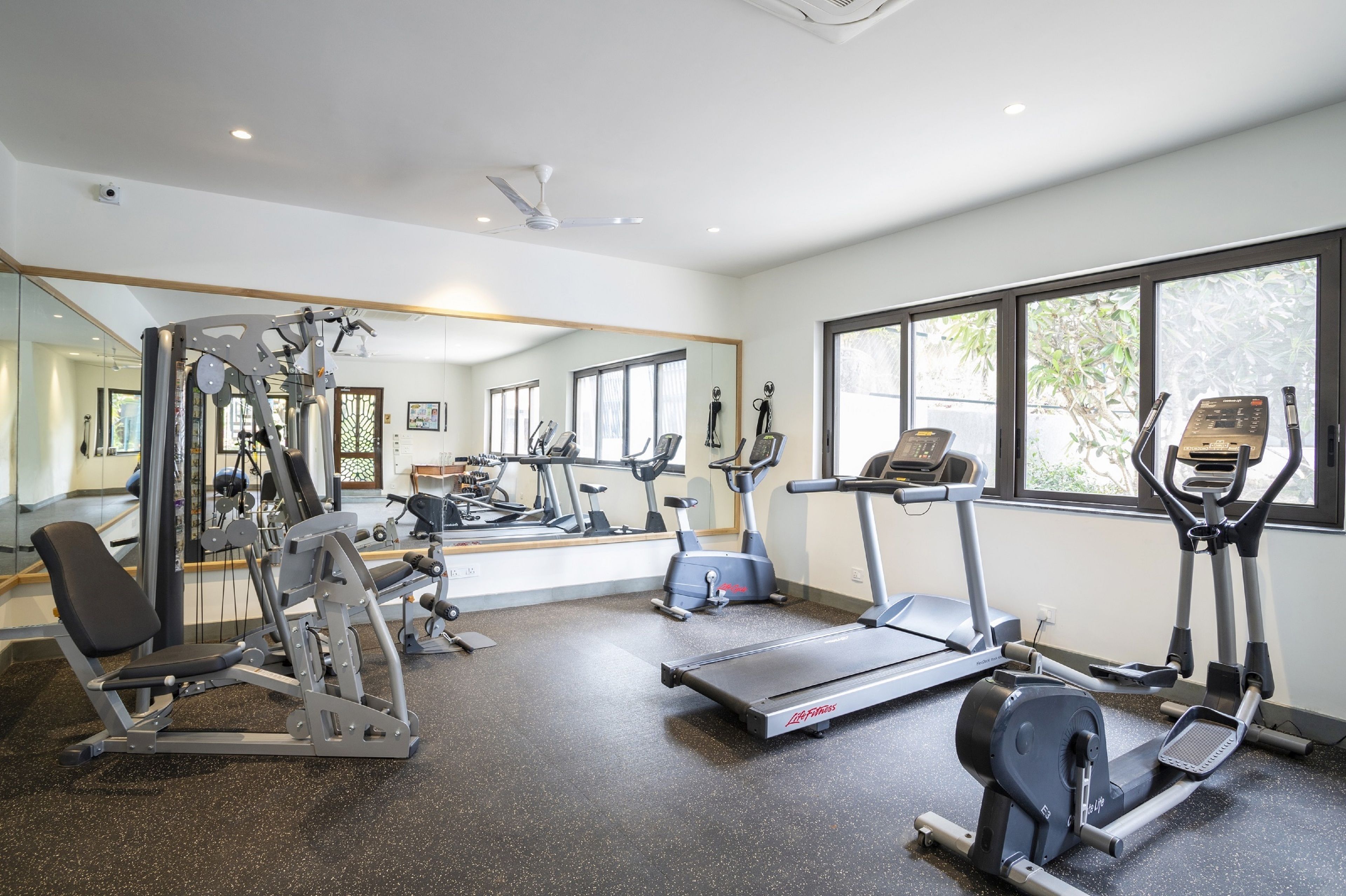 Een sportschool met diverse fitnessapparaten, grote ramen en een spiegel.