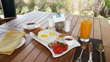 A breakfast table with a plate of eggs, toast, and tomatoes, a glass of orange juice, and a small plant with a name tag.