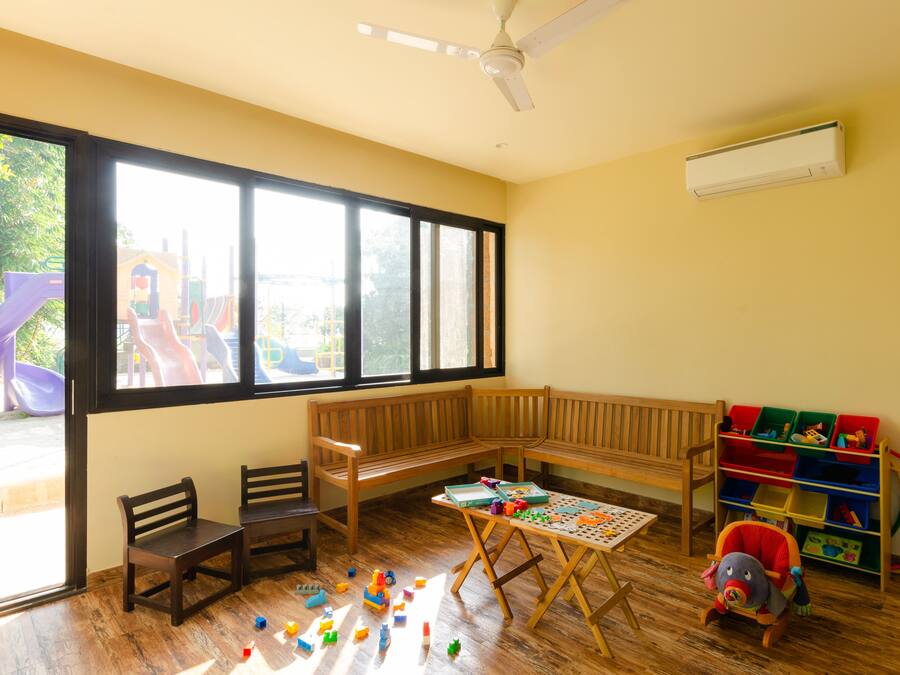 Una habitación con un ventanal amplio, un banco de madera, una mesa con juguetes y un área de juegos visible desde fuera.