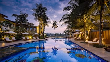 Relax by the serene pool surrounded by lounge chairs and umbrellas, overlooking a colorful mosaic design.
