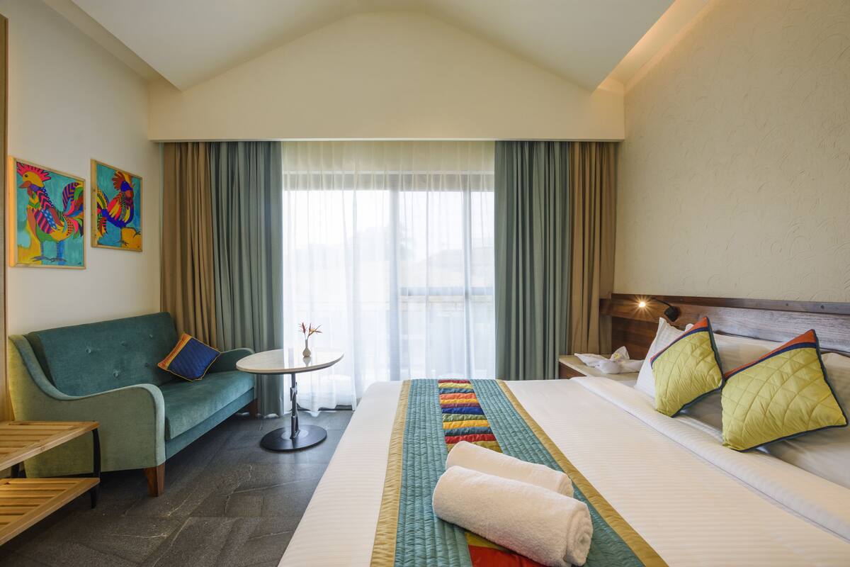 A hotel room with a bed, a sofa, a small table, and two paintings on the wall.