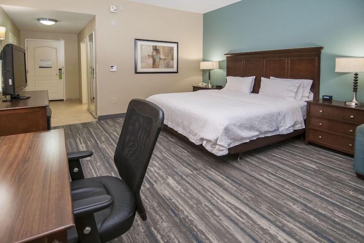 Habitación de hotel con una cama grande, un escritorio con silla, un televisor y una puerta que da a otra habitación.