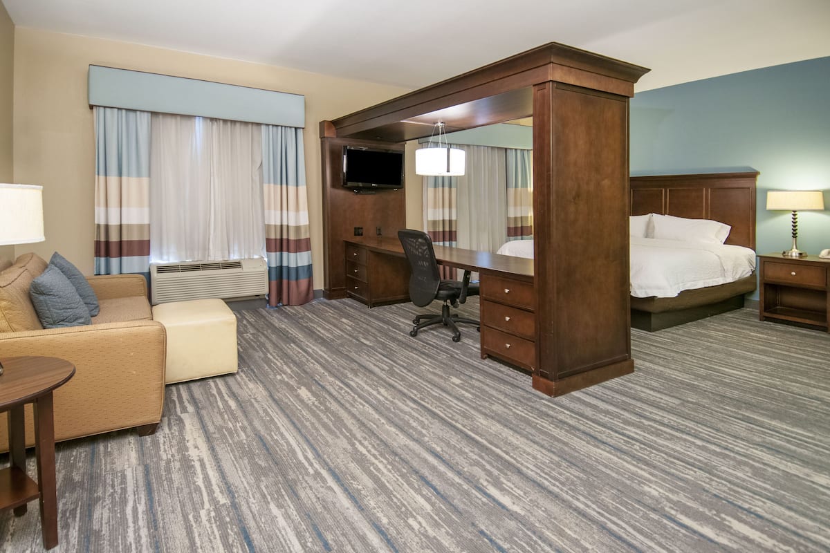 Una habitación de hotel con cama, escritorio con silla, sofá, televisión y un espejo grande.