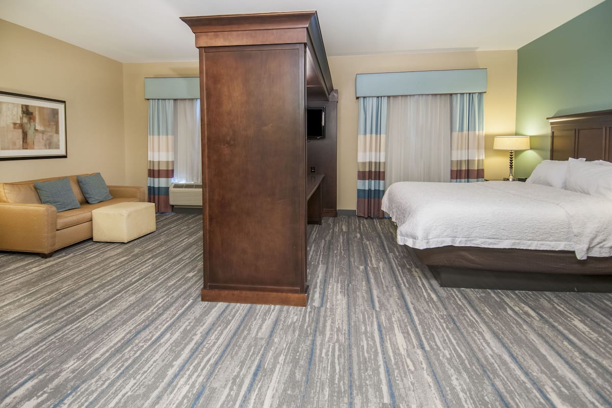 Una habitación de hotel con cama, sofá, un pilar de madera y un cuadro en la pared.