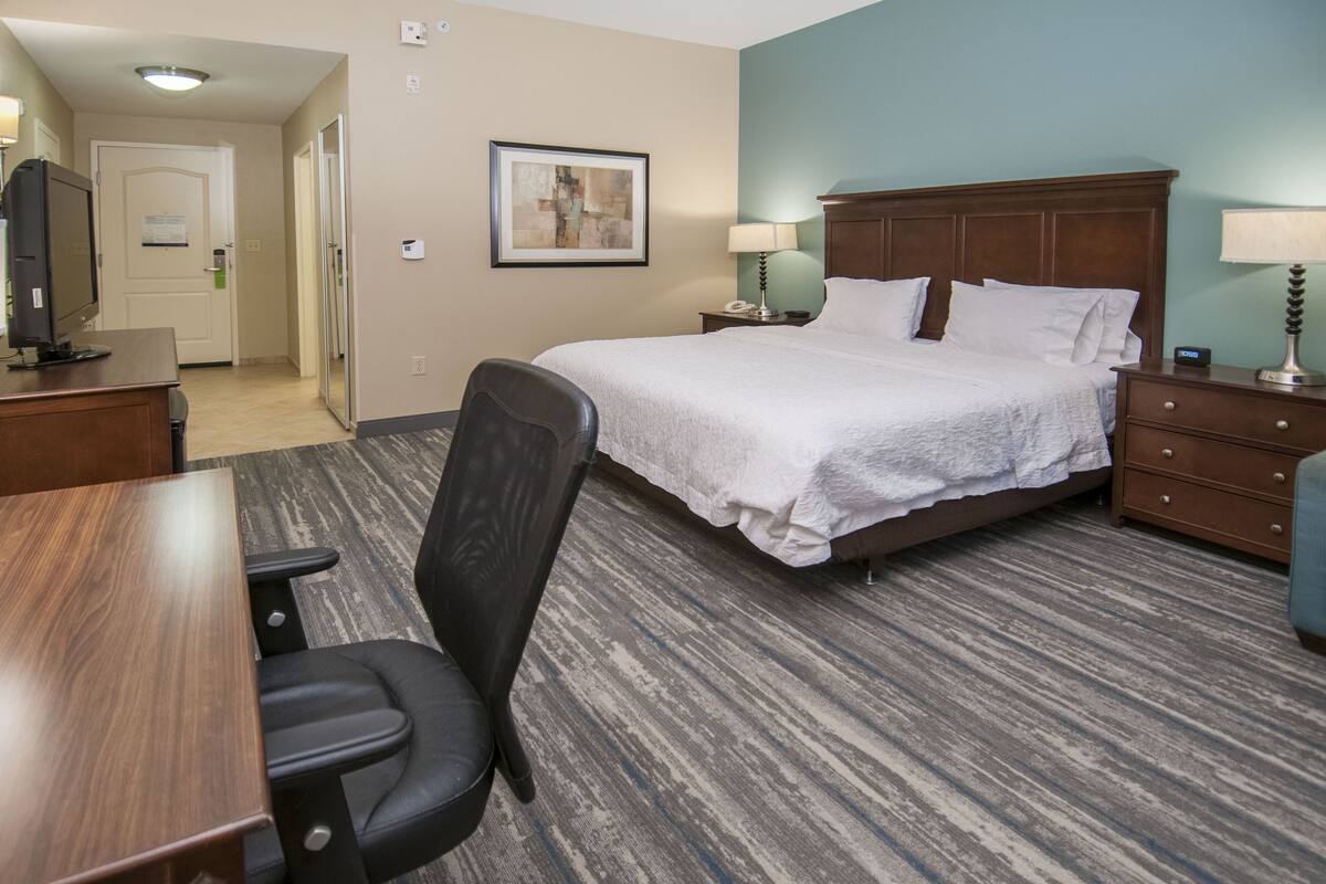 Habitación de hotel con una cama grande, un escritorio con silla, una mesita y una lámpara.