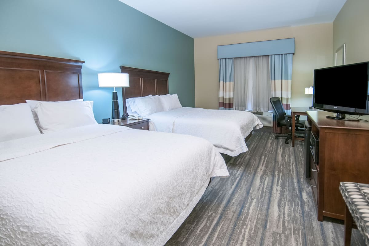 Habitación de hotel con dos camas, un escritorio con televisor y una silla.