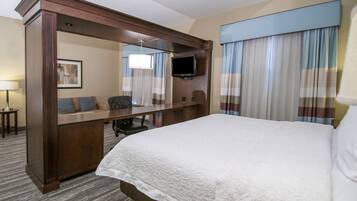Habitación de hotel con una cama grande, un escritorio con una silla, un televisor y una ventana con cortinas.