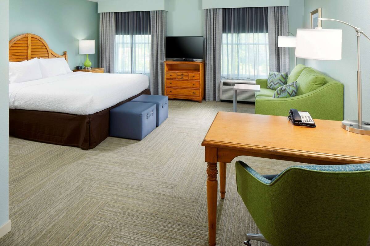 A hotel room with a bed, a desk, a chair, a TV, and a telephone.