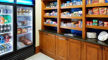 A refrigerated beverage cooler with various drinks and a shelf stocked with snacks and packaged goods.