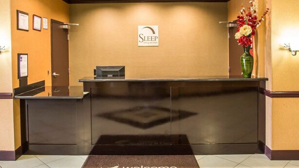 A reception desk with a "Sleep Inn & Suites" sign, a reception counter, a door, and a wall-mounted vase with flowers. - Sleep Inn & Suites Abilene Near University (Abilene)
