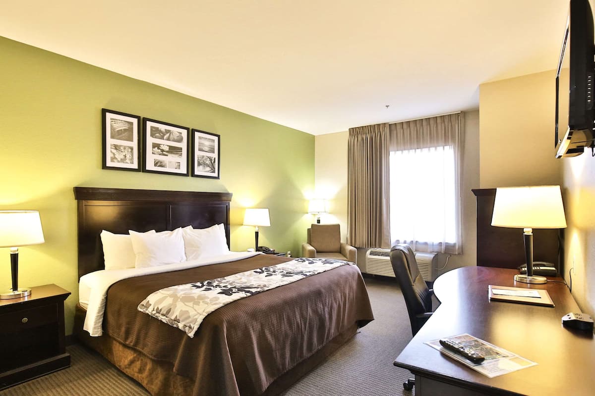 Une chambre d’hôtel avec un grand lit, deux tables de chevet avec des lampes, un bureau avec une chaise, une télévision et des tableaux encadrés au mur.