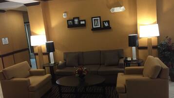 A hotel lobby with a sofa set, two side tables with lamps, a coffee table with flowers, and framed pictures on the wall.