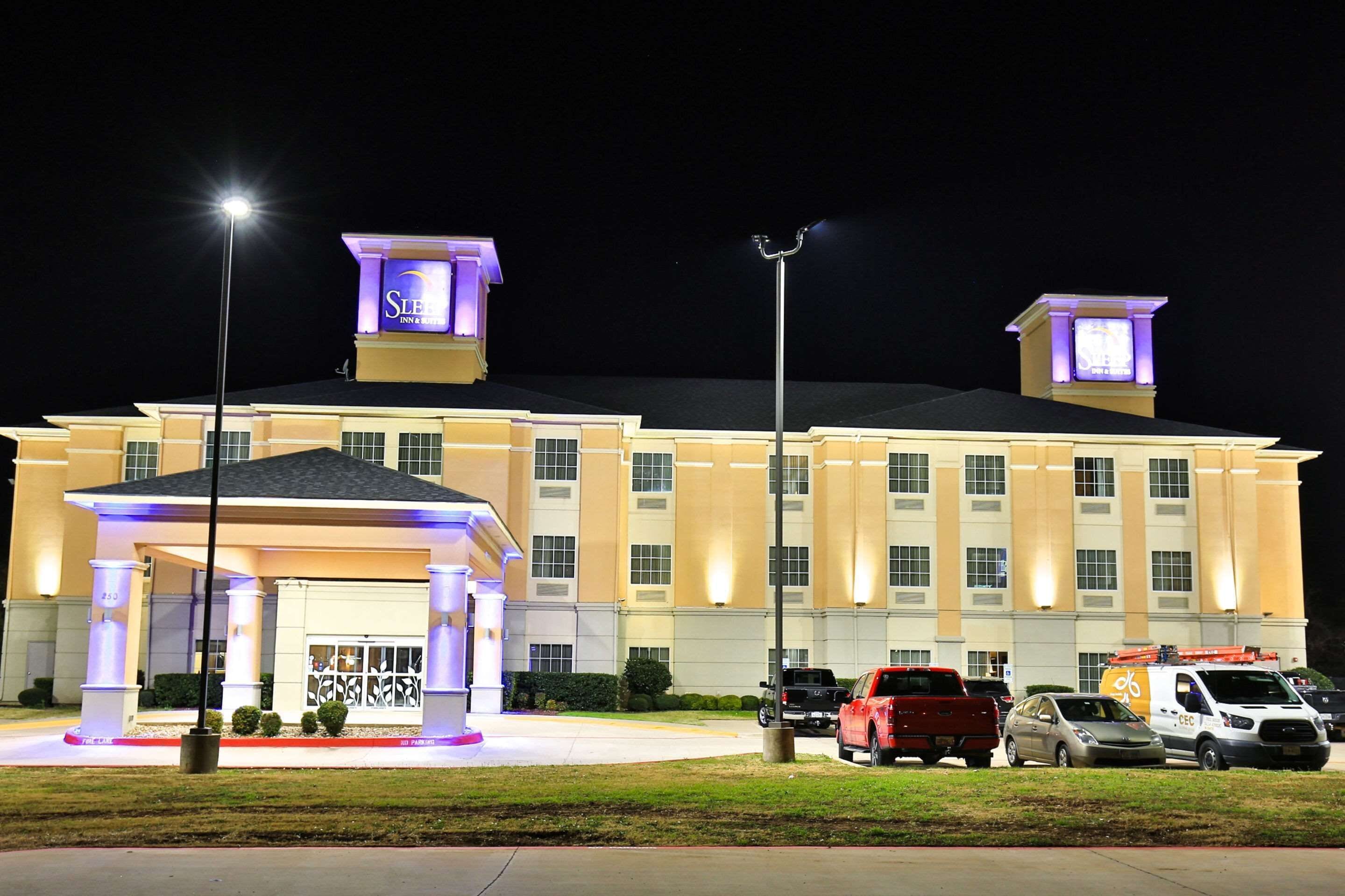 A hotel with a prominent entrance, multiple parking spaces, and a well-lit facade.