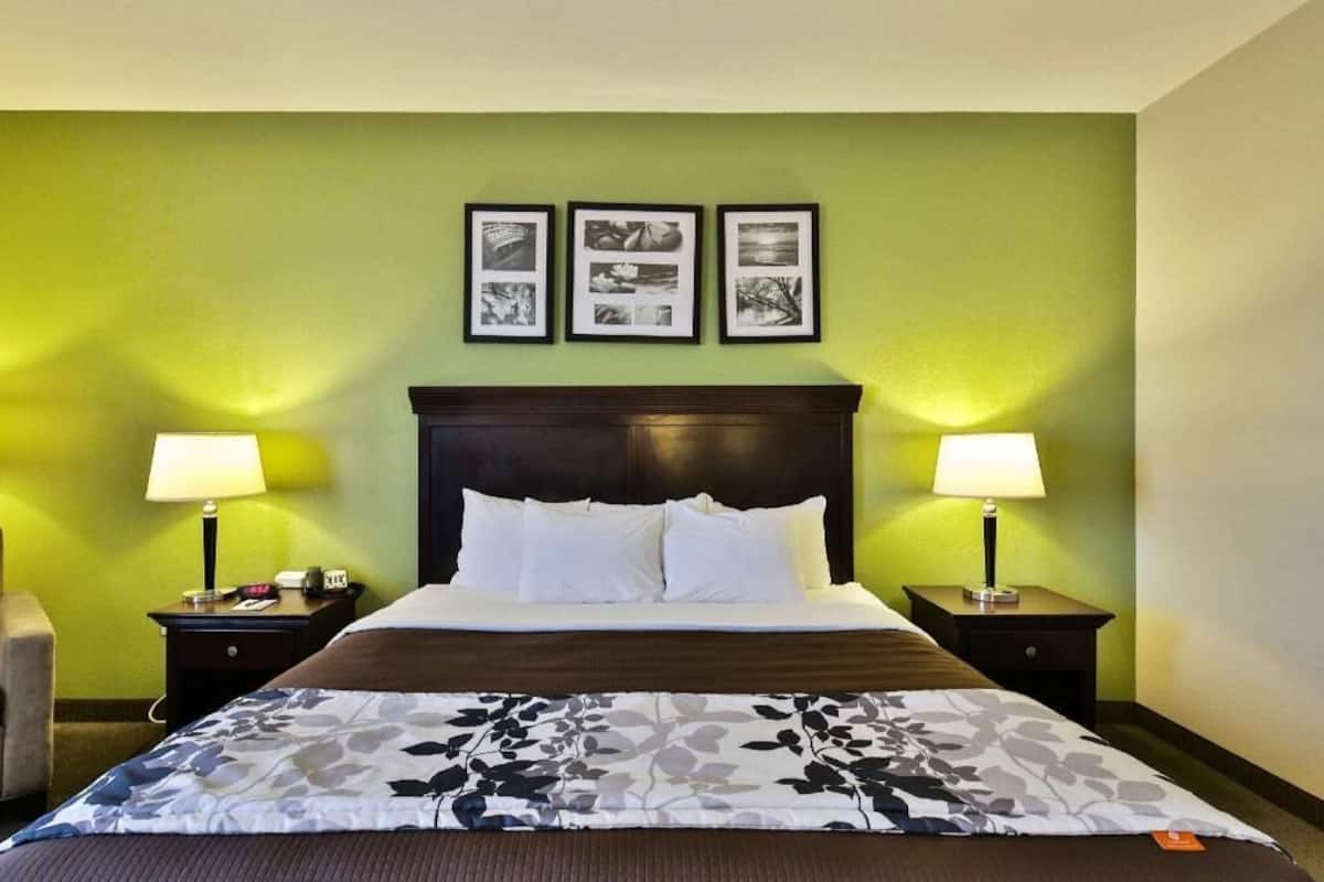 Une chambre d’hôtel avec un lit, deux tables de chevet, une chaise et trois tableaux encadrés accrochés au mur.