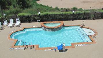 A swimming pool with a brick edge, a diving board, and lounge chairs.