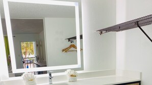 Un baño con un lavabo blanco, un espejo con luz, un perchero y un estante con toallas.