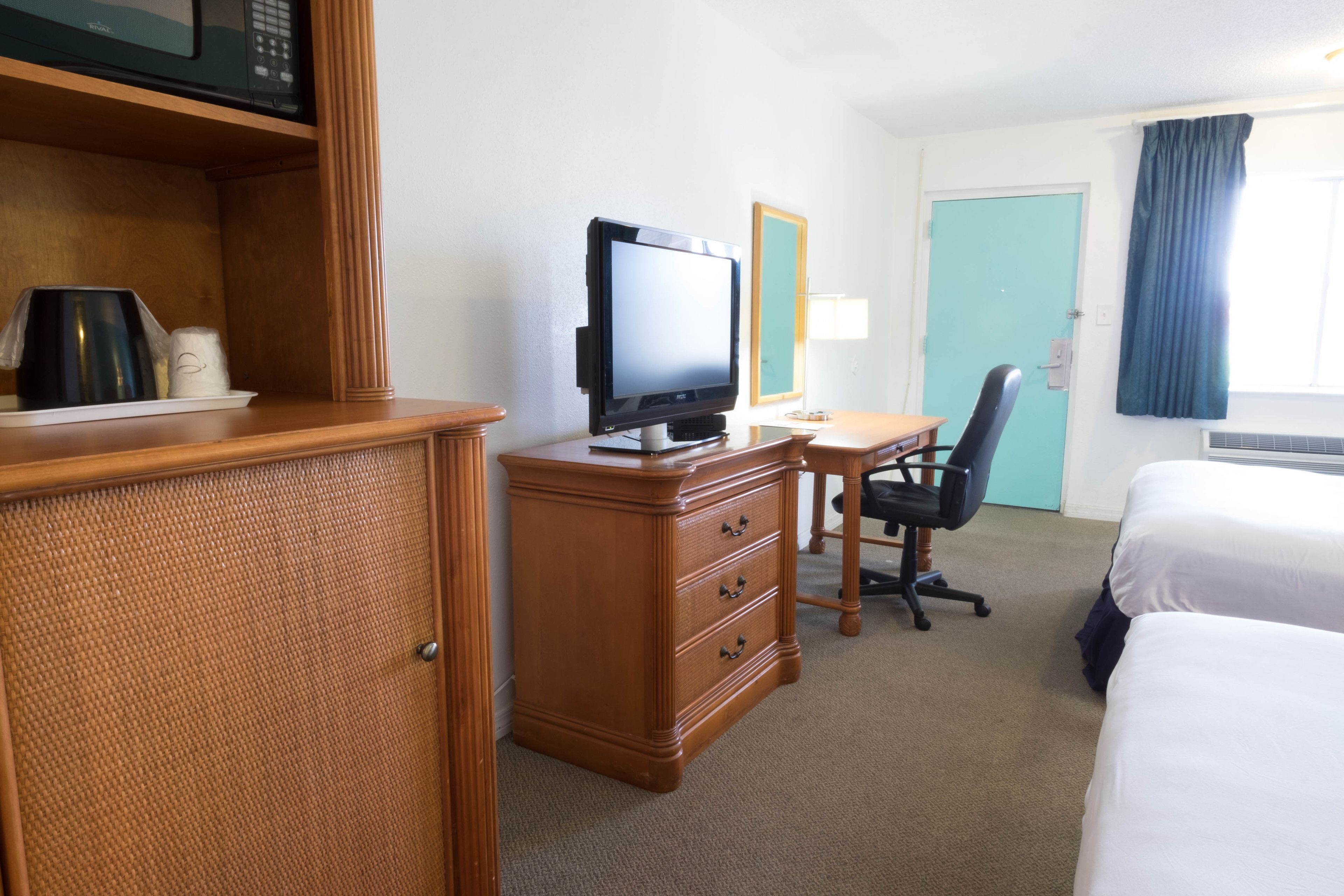 Una camera d'albergo con un comò in legno, una televisione, una scrivania con una sedia e due letti.