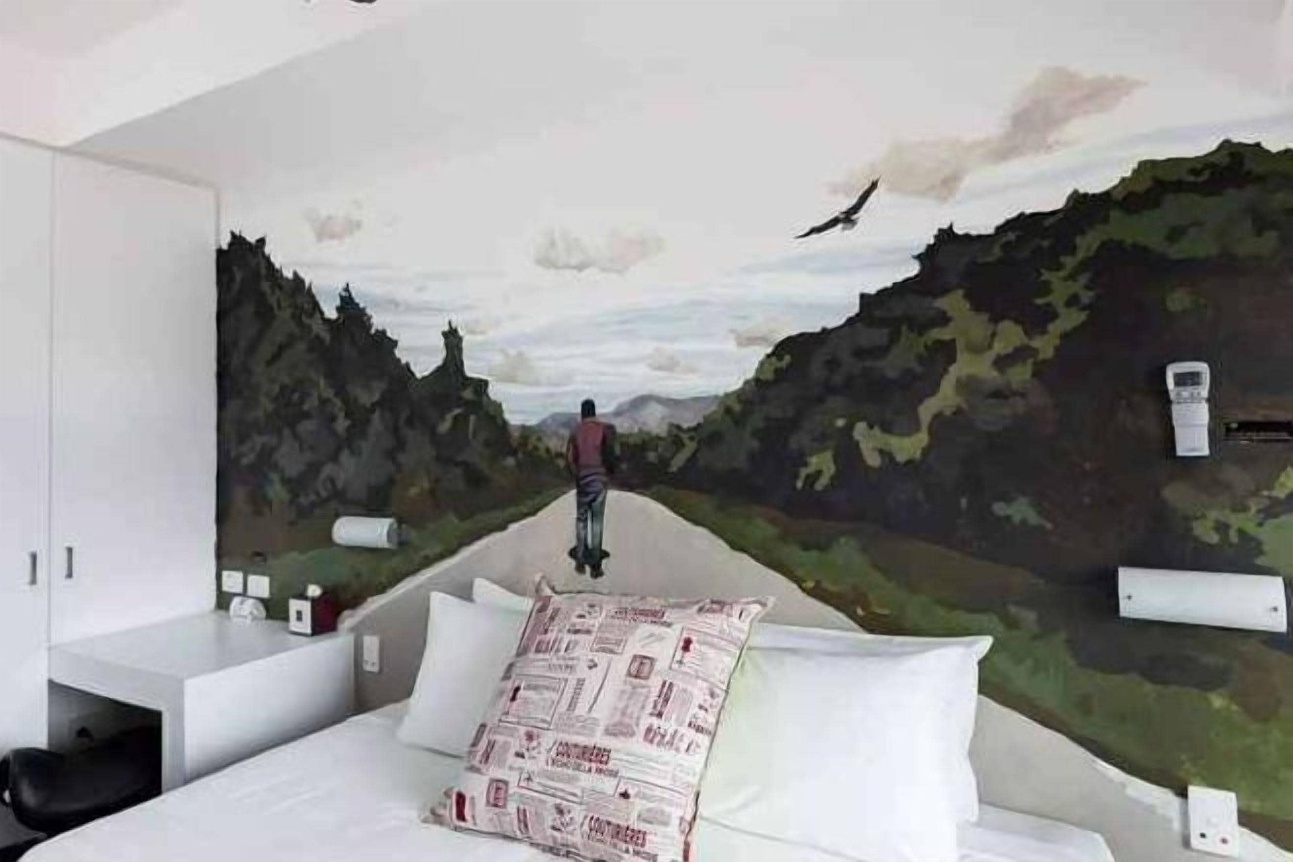 A bedroom with a mural of a landscape, a bed, a desk, and a chair.