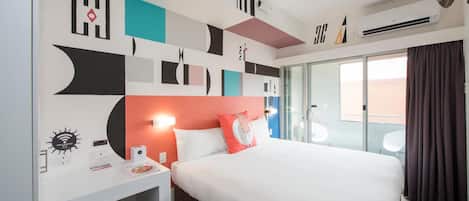 Habitación de hotel con cama, escritorio y silla. Se ve una ventana con cortinas, un reloj de pared y un televisor de pantalla plana montado en la pared.