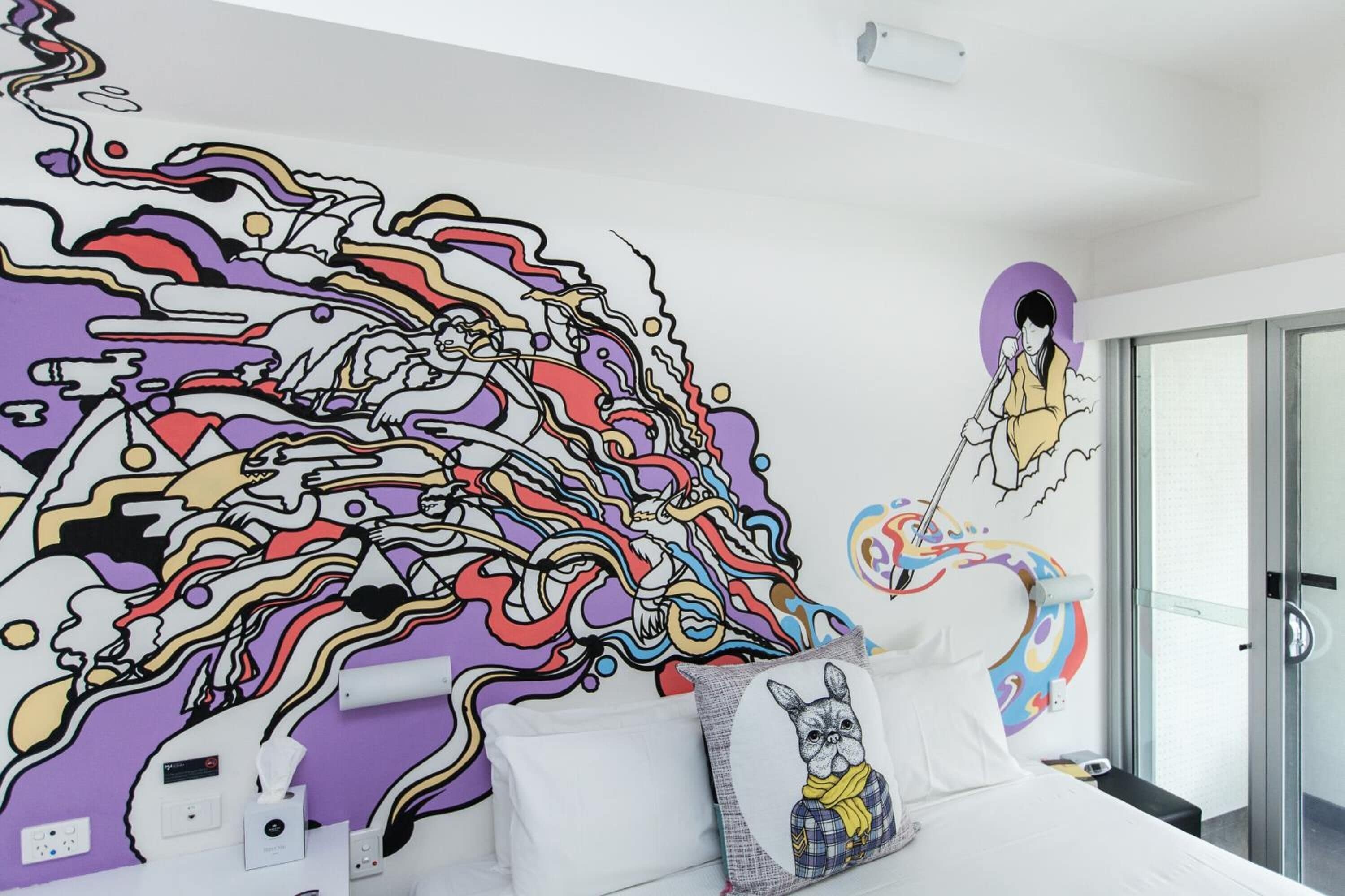 A modern hotel room with a large abstract mural on the wall, a bed with white linens, and a glass shower door.