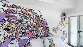 A modern hotel room with a large abstract mural on the wall, a bed with white linens, and a glass shower door.