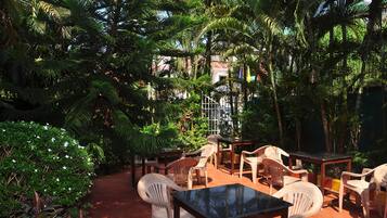 An outdoor seating area with tables and chairs, surrounded by lush greenery and palm trees.