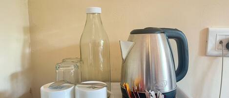 A tray with a stainless steel kettle, a glass bottle, and two white mugs on a white surface.