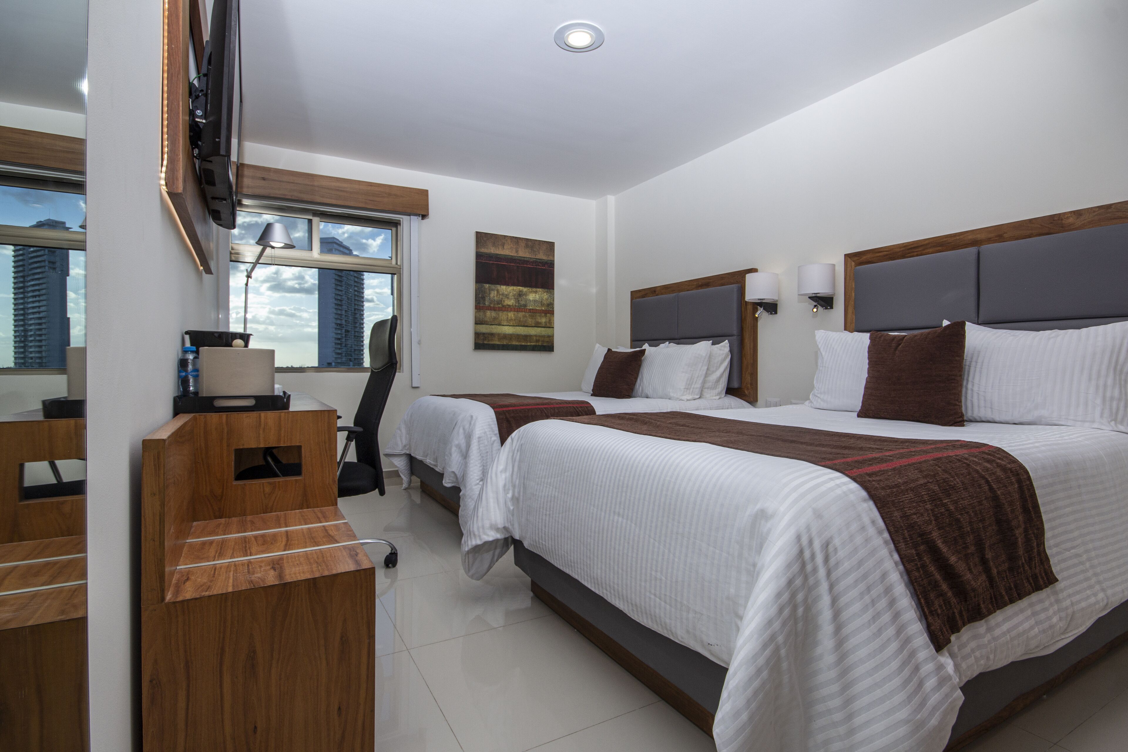 A hotel room with two beds, a desk, and a TV mounted on the wall.