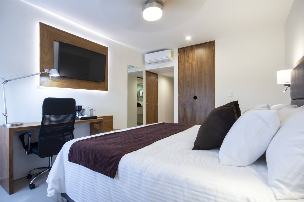 A hotel room with a bed, desk, chair, and a television mounted on the wall.
