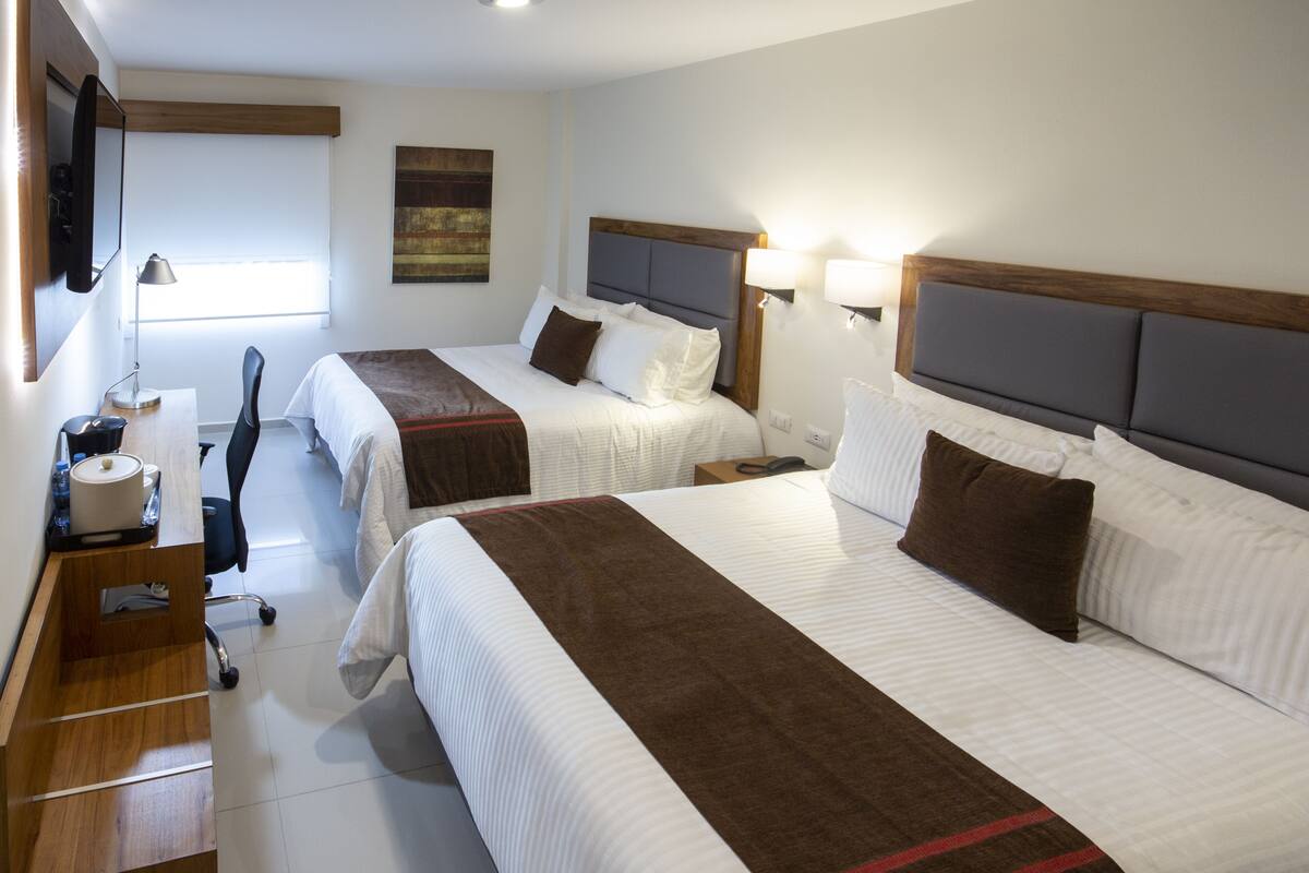 A hotel room with two beds, a desk, a chair, a TV, and a window.