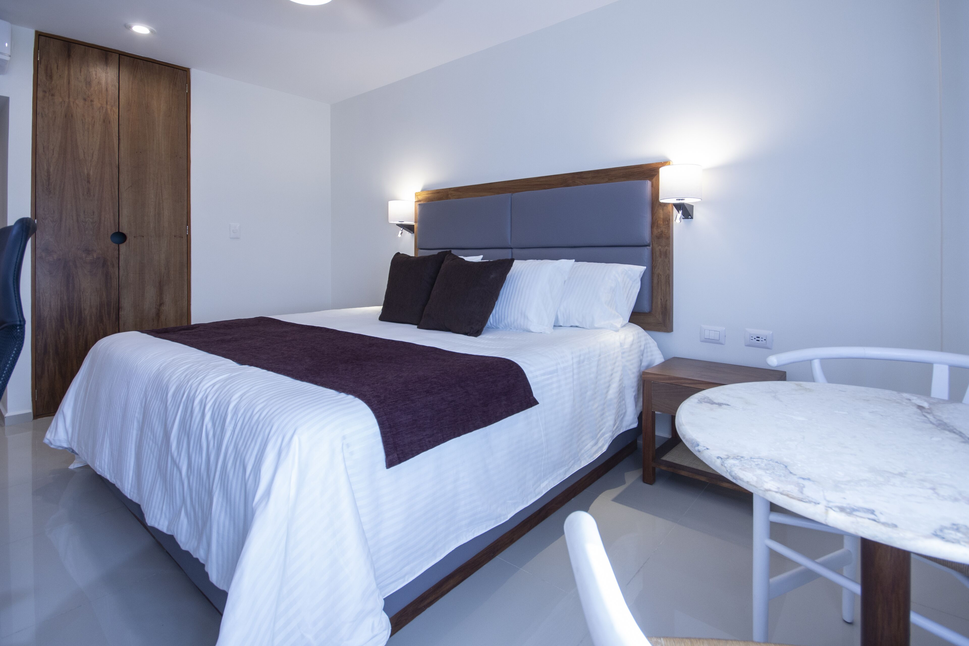 Un dormitorio ordenado con una cama, una mesita de noche y una pequeña mesa redonda.