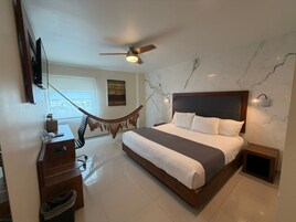 Un dormitorio con cama, escritorio, silla, ventilador de techo y vistas al exterior.