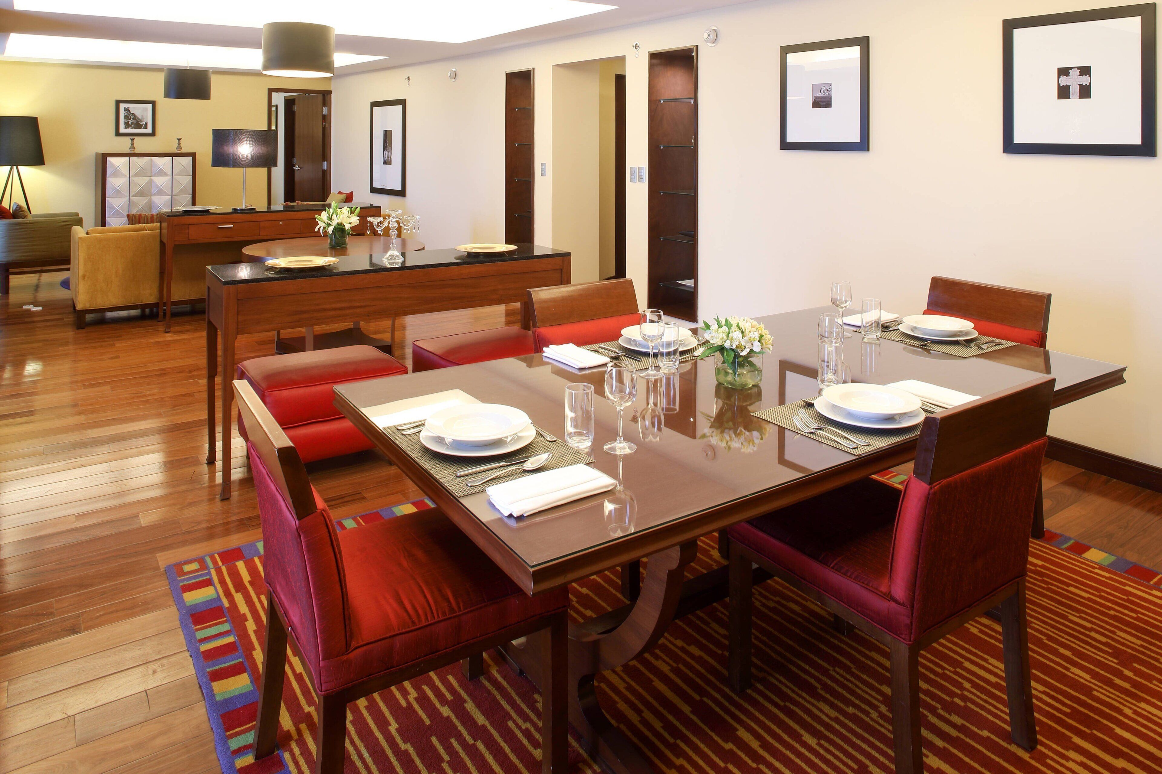 Comedor con una mesa de madera dispuesta para cuatro comensales, sillas tapizadas en rojo y un mostrador de buffet al fondo.