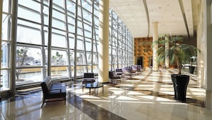 A spacious lobby with large windows, a seating area with sofas and tables, and a large potted plant.