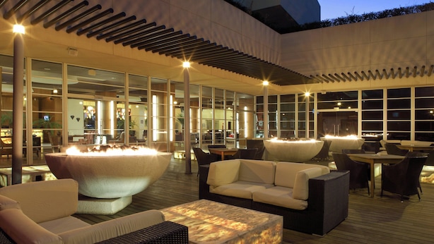 An outdoor lounge area with a large heated water feature, comfortable seating, and a glass-enclosed interior.