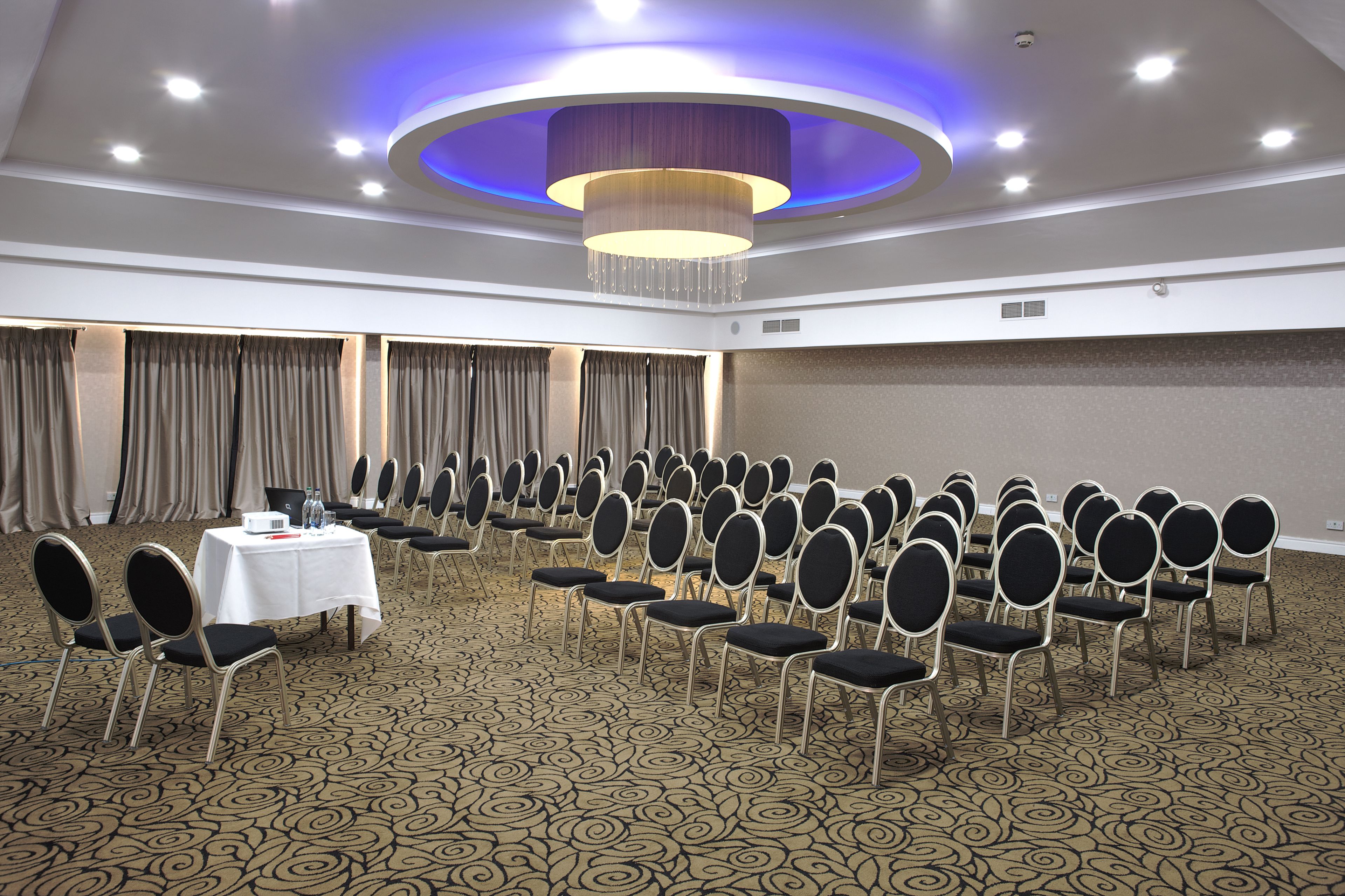 Ein Konferenzraum mit Reihen von Stühlen, einem Tisch mit Wasserflaschen und einem Kronleuchter.
