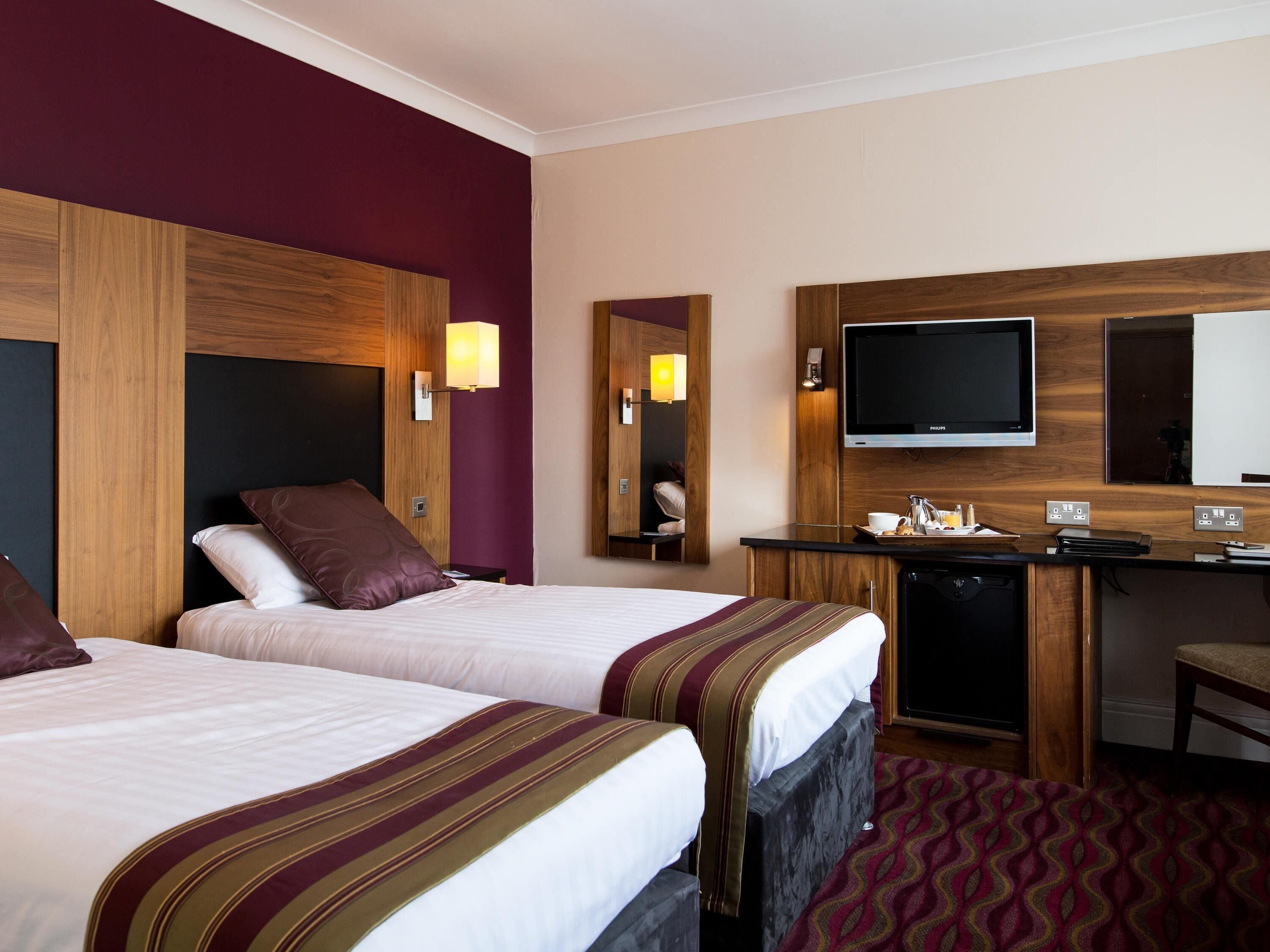 A hotel room with two beds, a desk, a television, and a mirror.