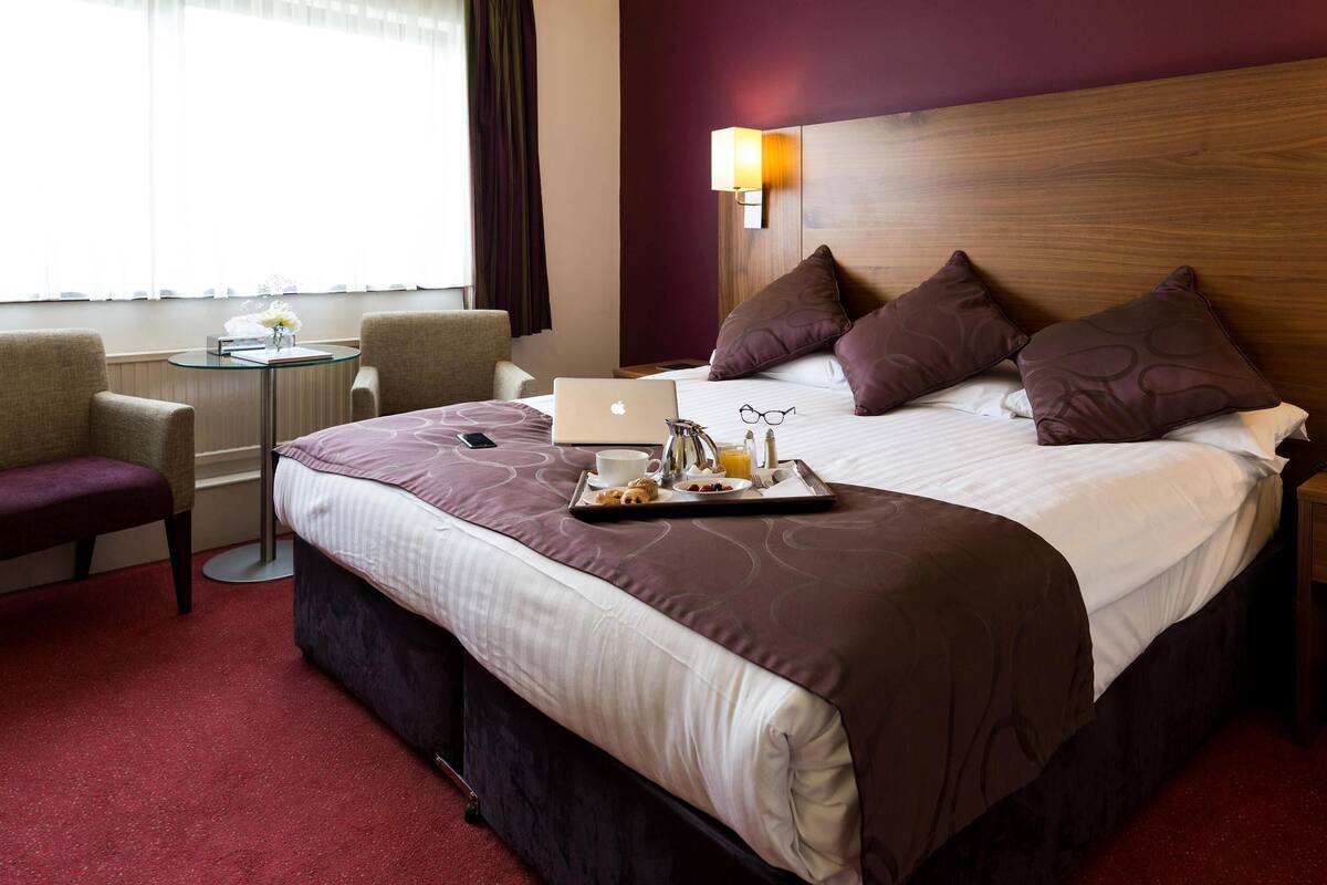 A hotel room with a bed, a laptop, a tray with breakfast items, a chair, and a small table.