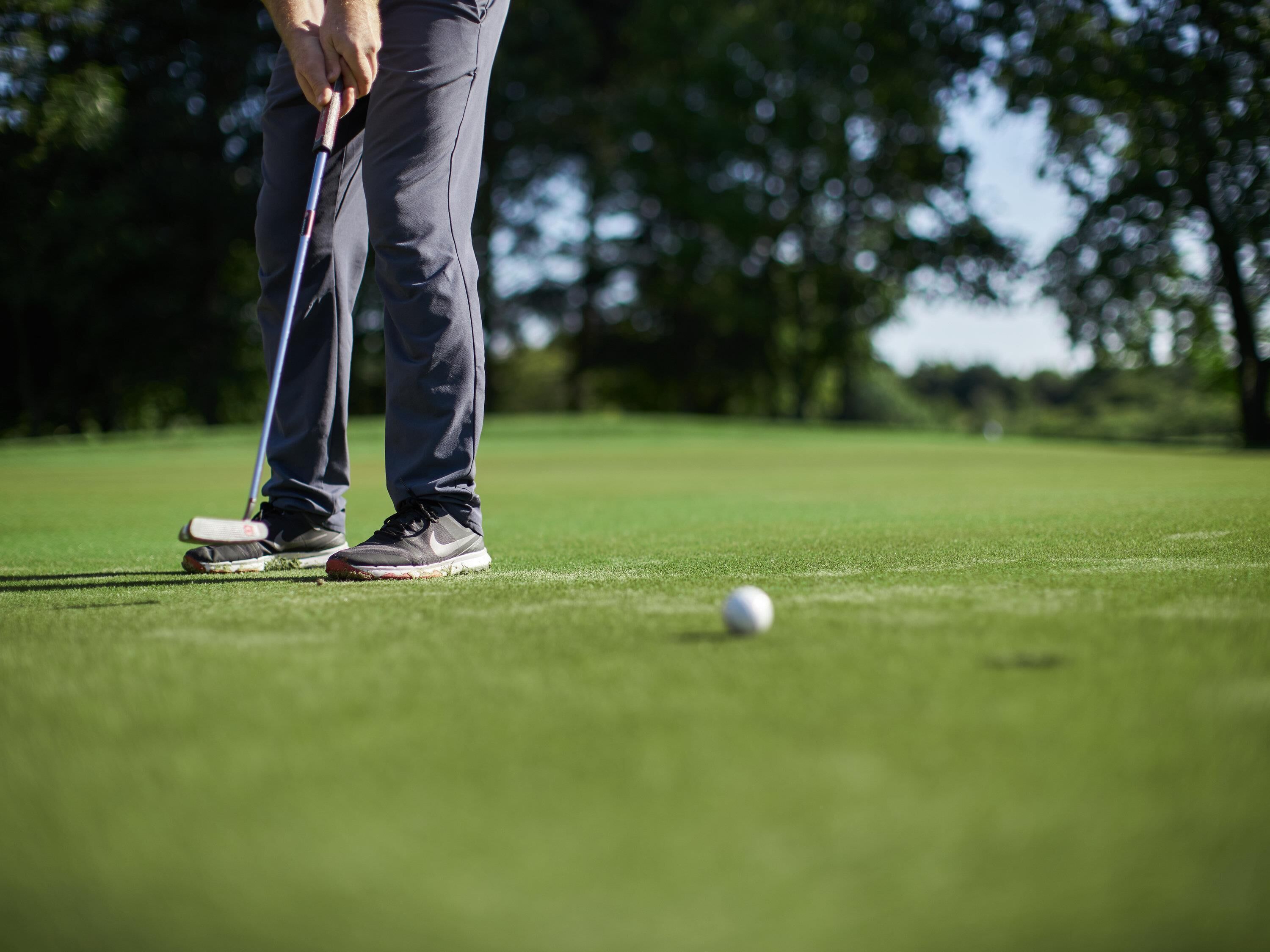 Una persona de pie en un campo de golf, sosteniendo un palo de golf y una pelota en el suelo.