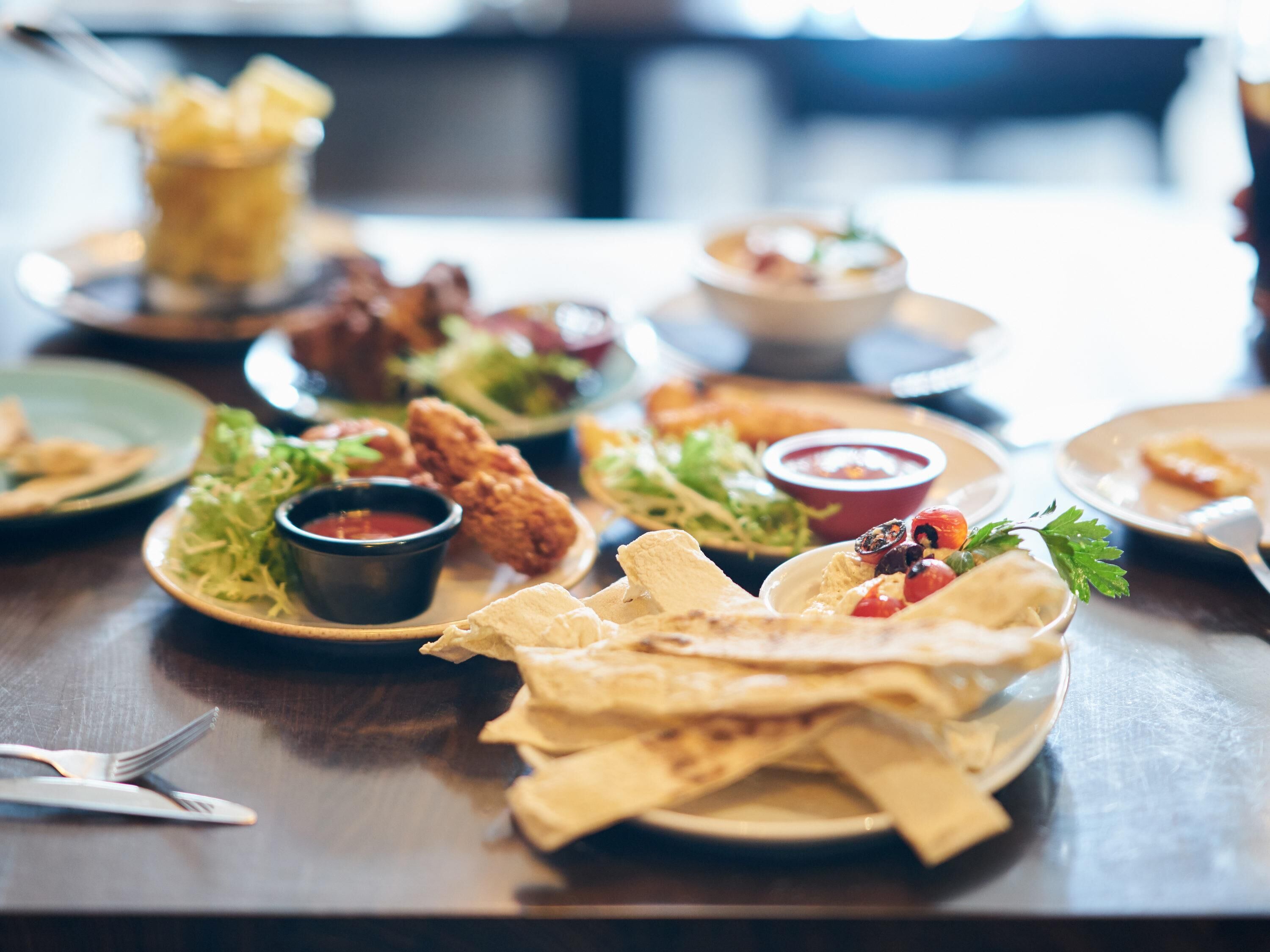 Une table à manger dressée avec divers plats, notamment du poulet frit, des salades et des galettes, ainsi que des condiments et des couverts.