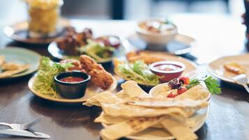 Une table à manger dressée avec divers plats, notamment du poulet frit, des salades et des galettes, ainsi que des condiments et des couverts.