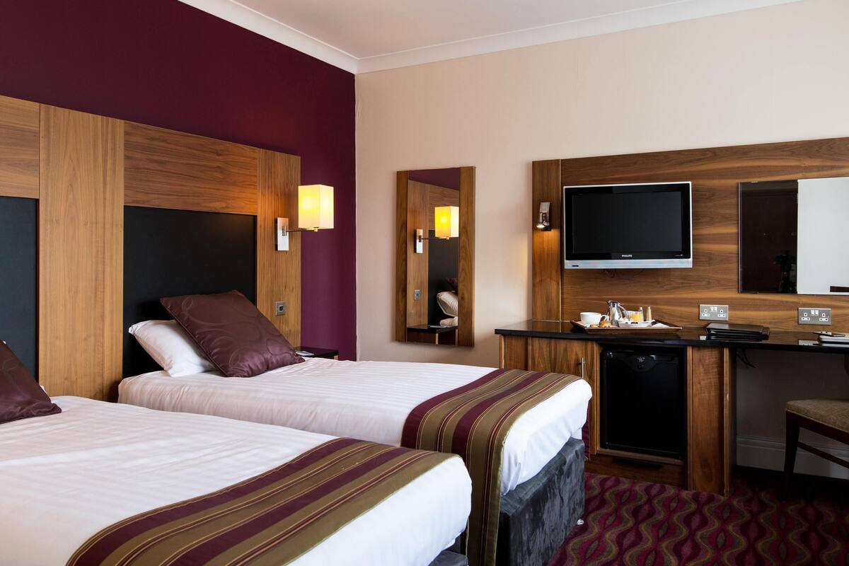 A hotel room with two beds, a desk with a television, and a mirror.
