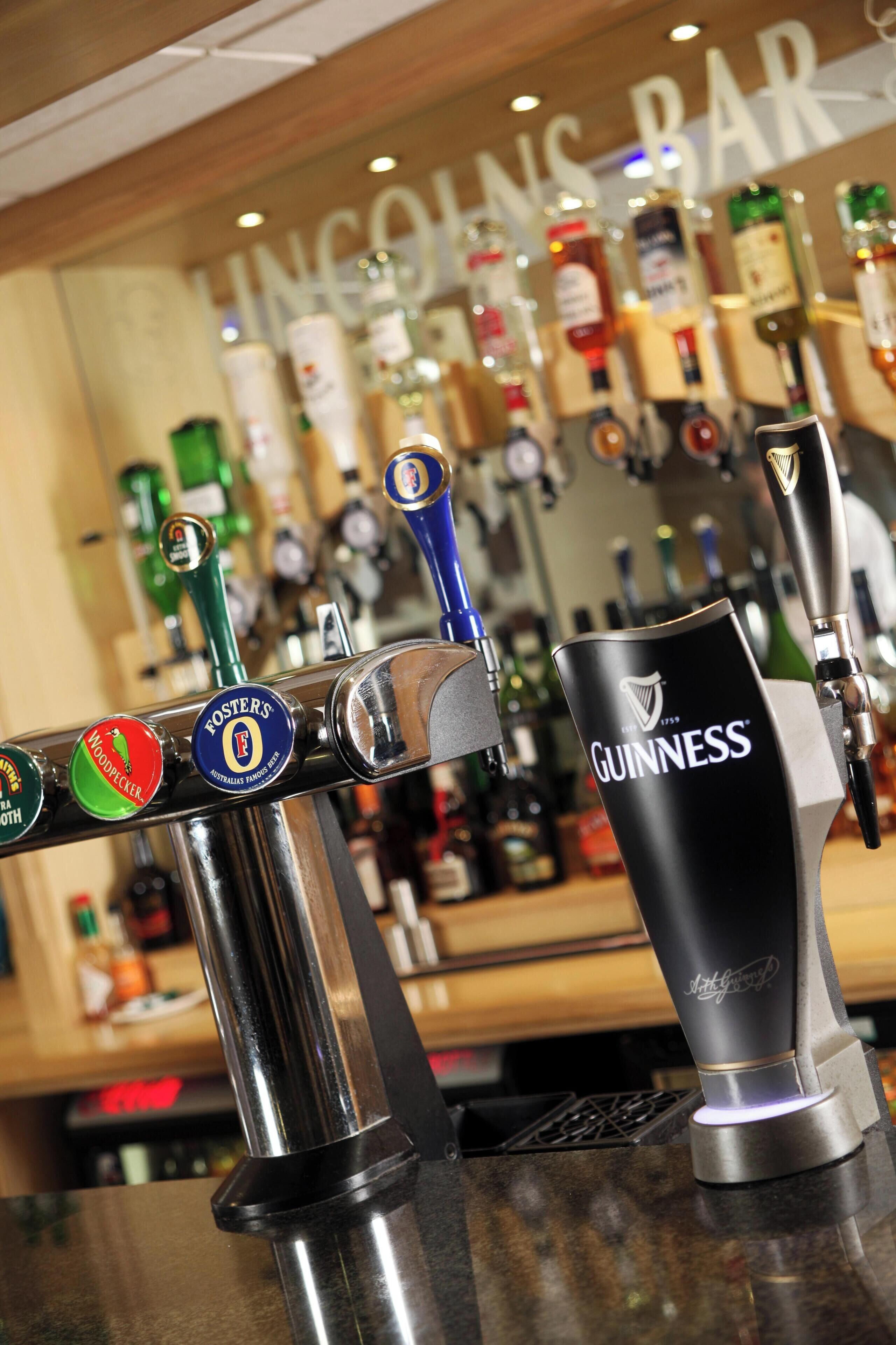 A bar counter with multiple beer taps, including brands like Woodpecker, Foster's, and Guinness.