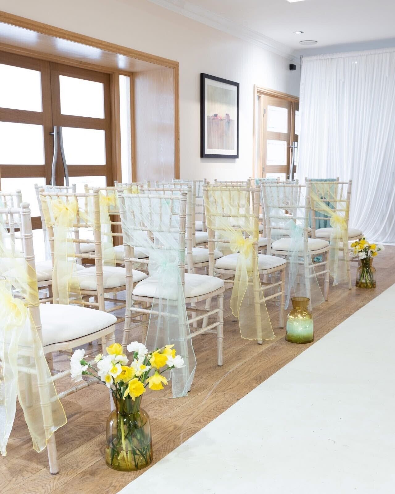 Una habitación con filas de sillas dispuestas para un evento, una larga mesa en el centro y un ventanal con vistas.